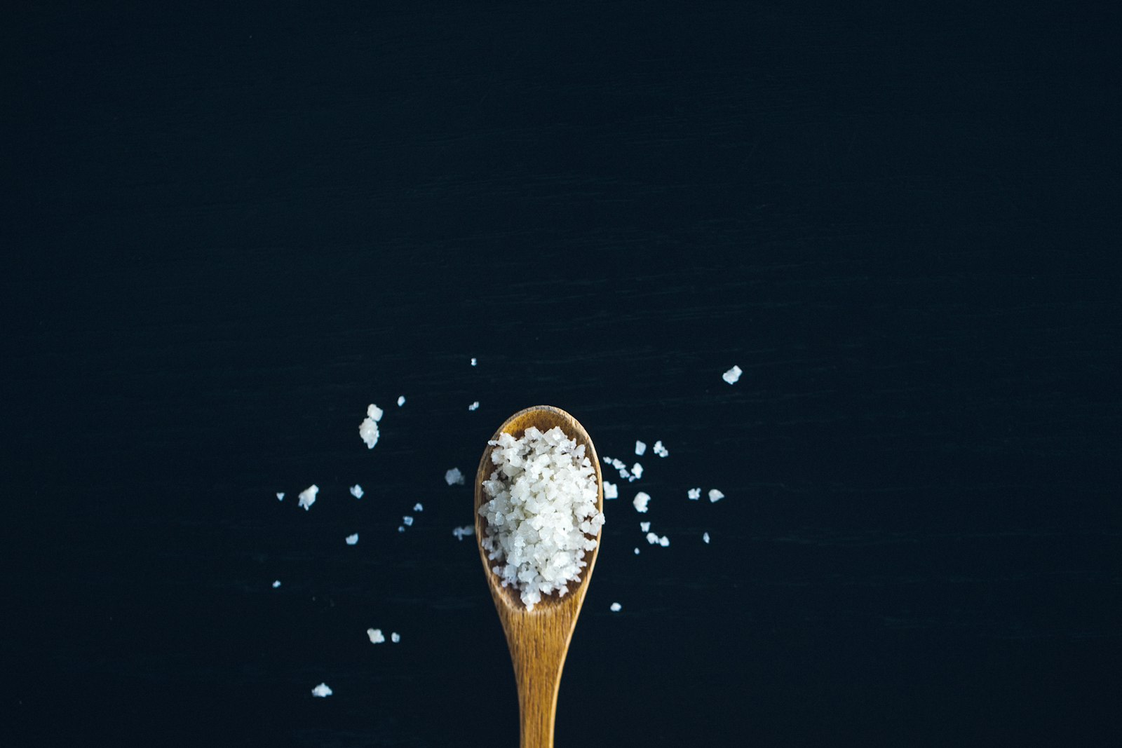 Coarse sea salt spilling from a small ceramic dish onto a dark surface